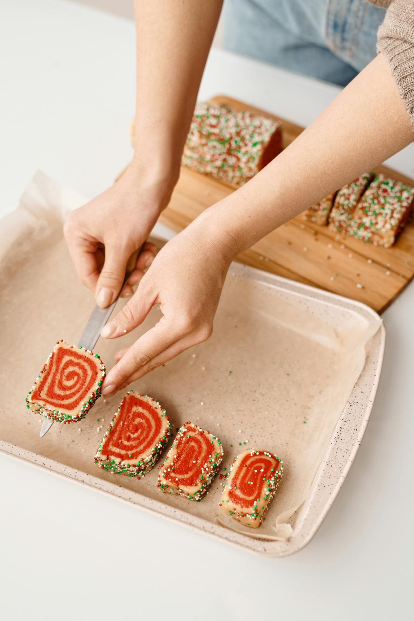 Sliced spiral cookies on a baking tray with colorful sprinkles, conveying festive vibes.